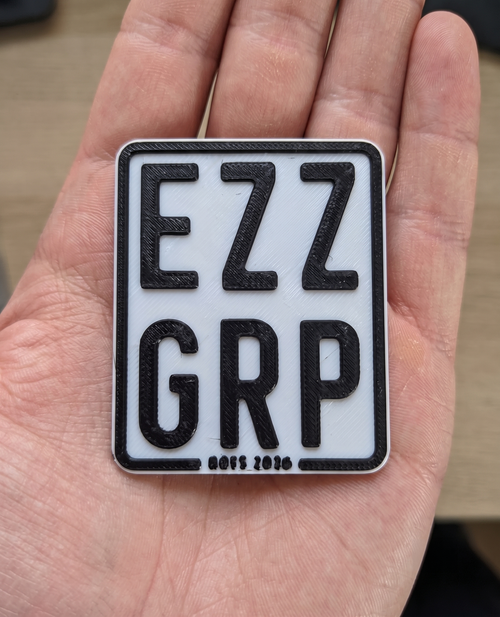 3D-gedrucktes E-Scooter-Deko-Kennzeichen mit Wunschtext EZZ GRP in der Hand - Groessenvergleich